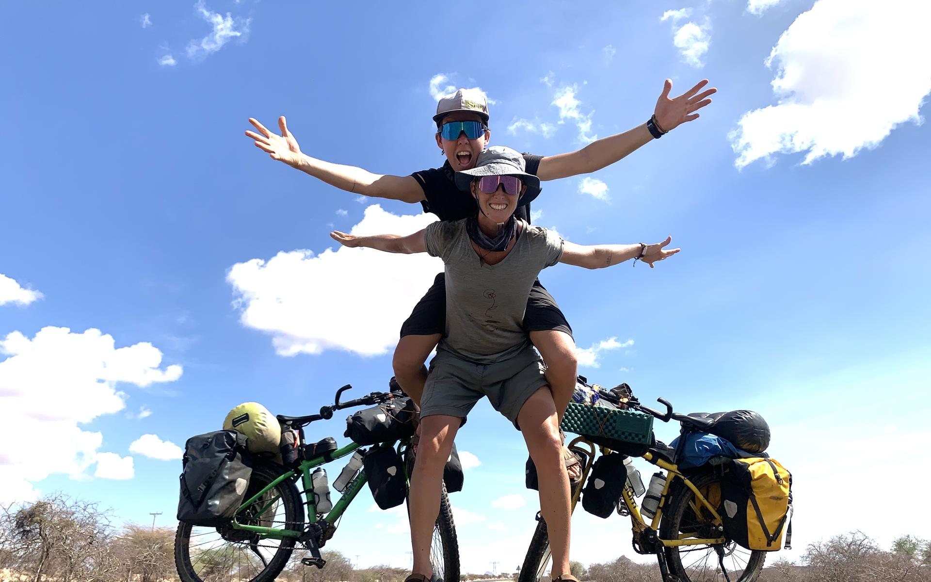2 Frauen, 2 Räder auf einer Straße, im Hintergrund Himmel
